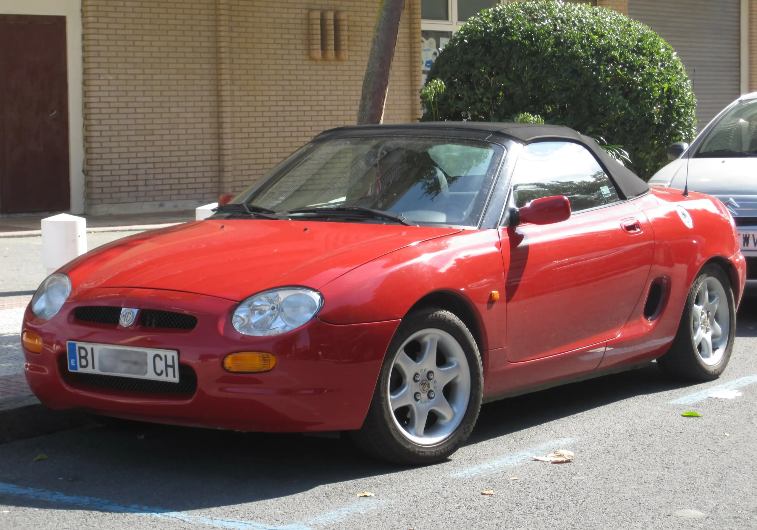 Red MG F convertible parked on a sunny, winding road.