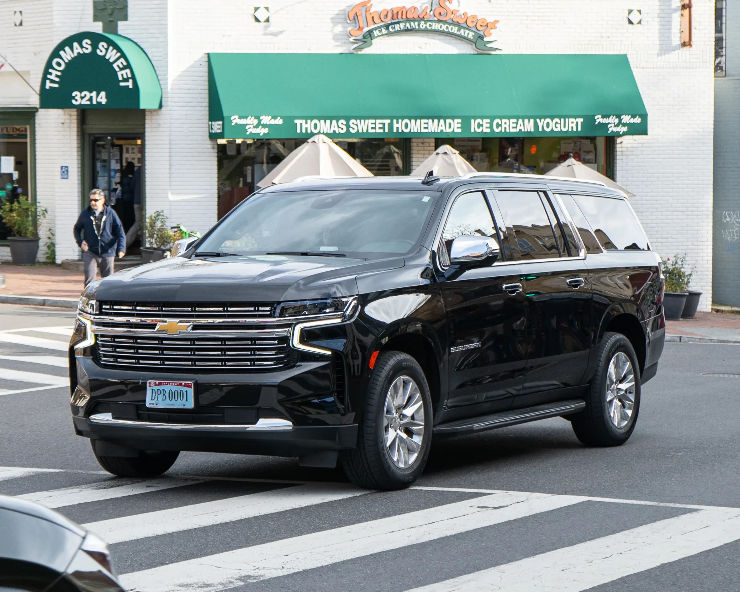 Silver Chevrolet Suburban parked on a sunny suburban street.