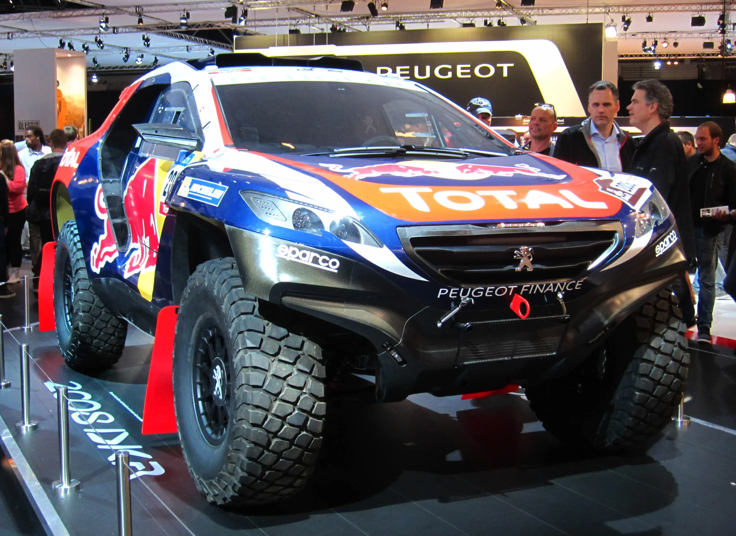 Red and white Peugeot 2008 DKR racing through a desert landscape.