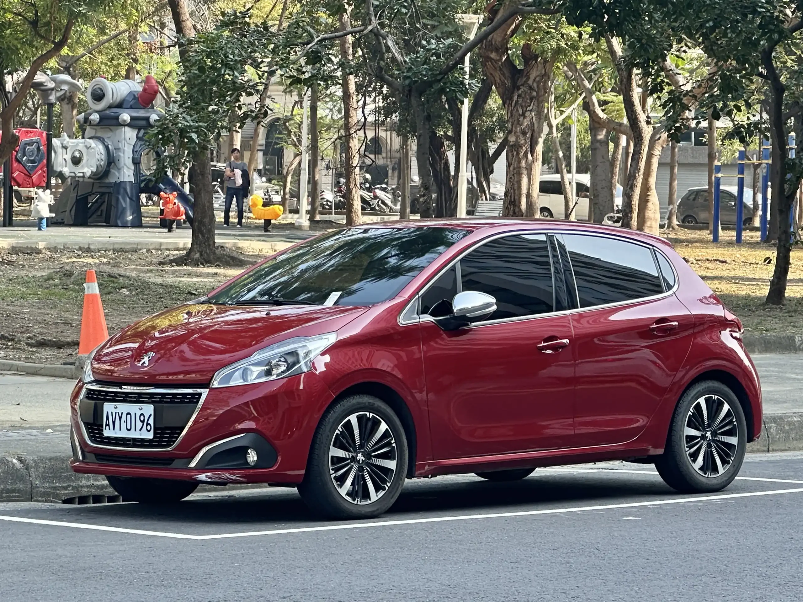 Red Peugeot 208 parked on a sunny city street.