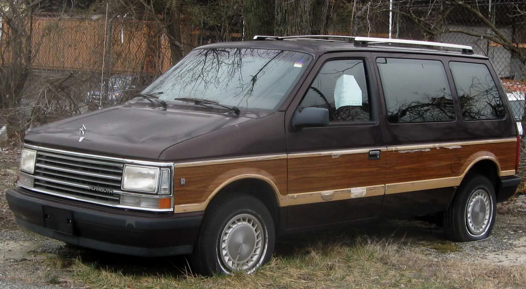 Silver 1990 Plymouth Voyager minivan parked on a sunny suburban street.