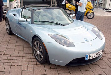  A light blue Tesla Roadster parked on a paved surface at an event, with a sleek convertible design and aerodynamic curves