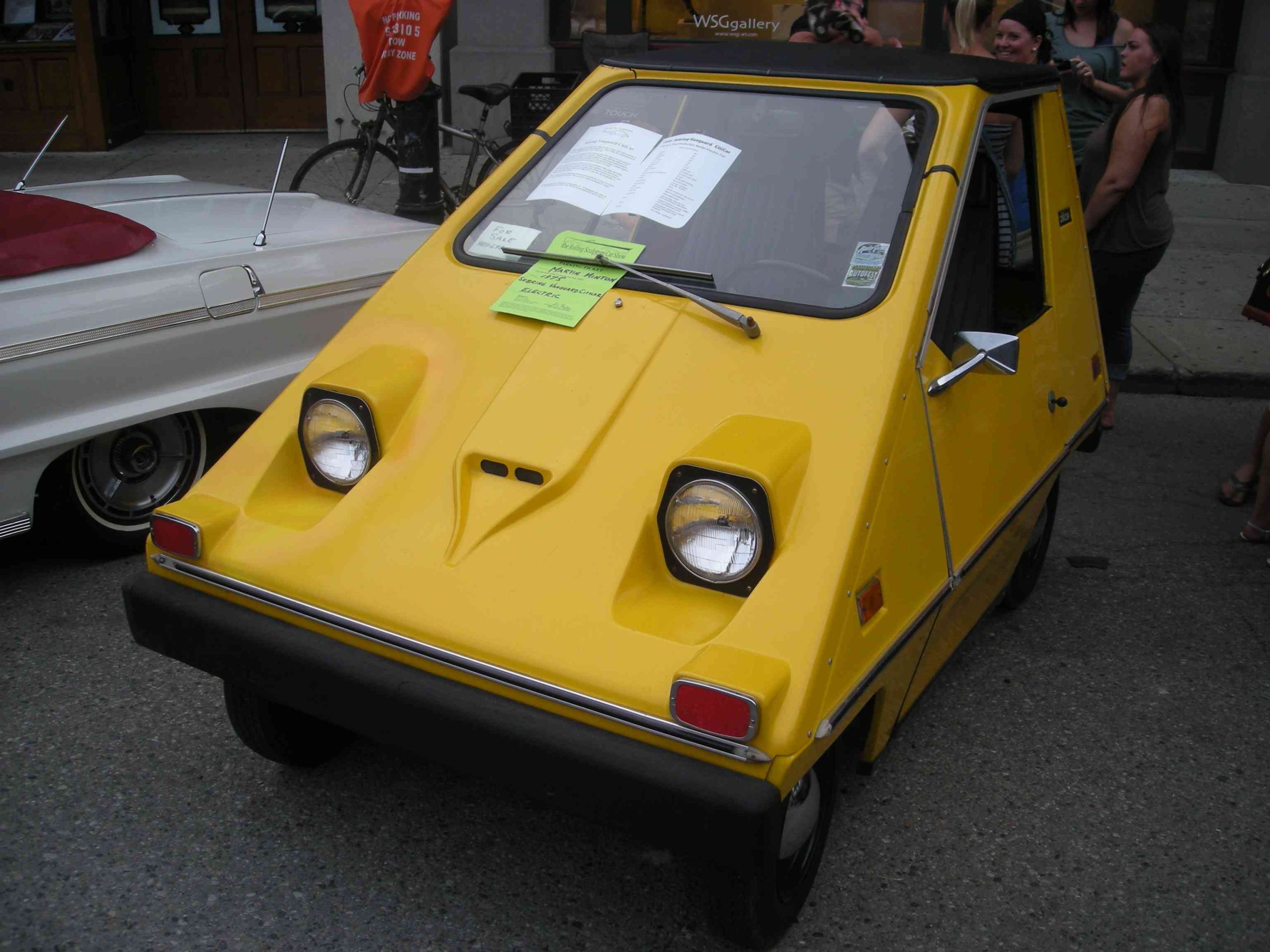 Small, yellow Sebring-Vanguard CitiCar electric vehicle parked on asphalt