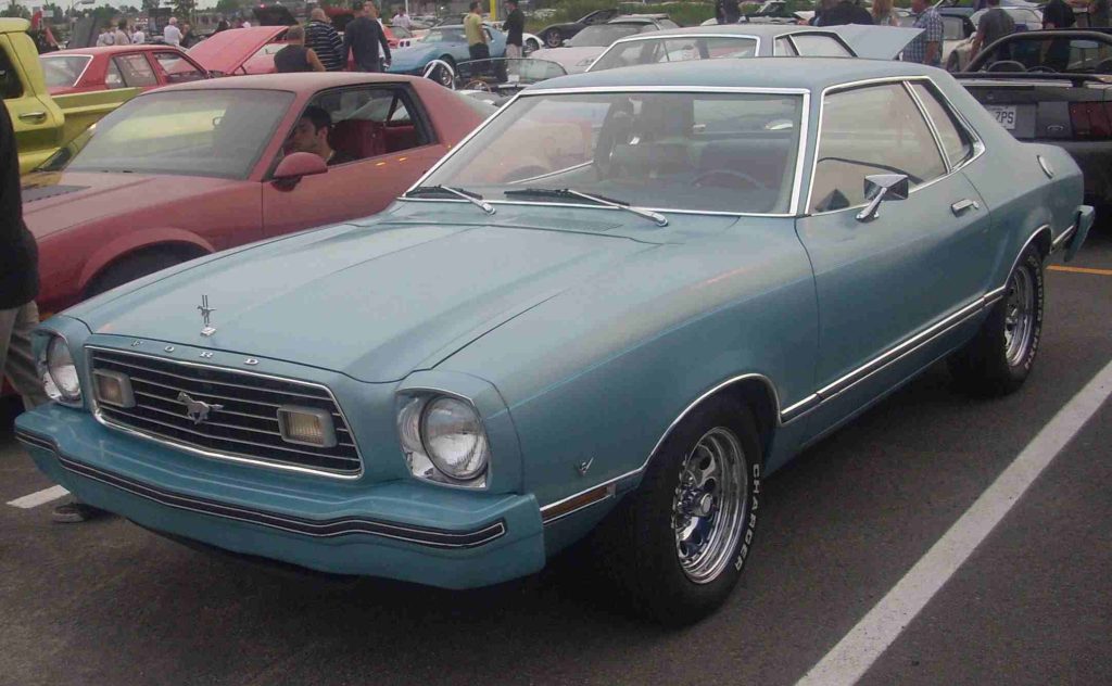 Side view of a yellow Ford Mustang II at a car show.

