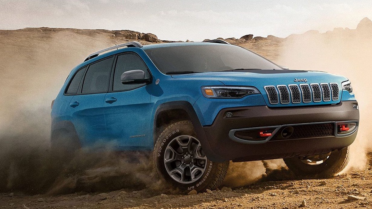 Blue Jeep Cherokee SUV with black wheel arches kicking up dust while driving on sandy desert terrain