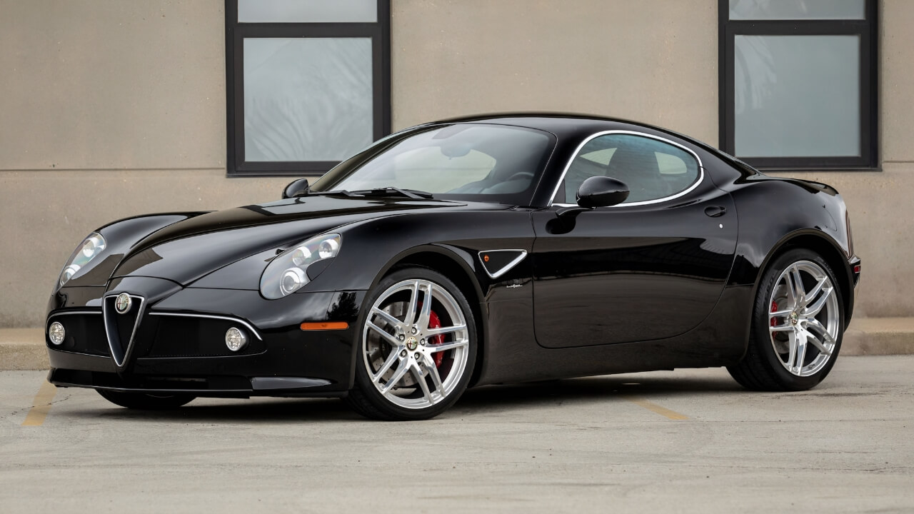 Black Alfa Romeo 8C Competizione sports car parked in front of modern building with large windows
