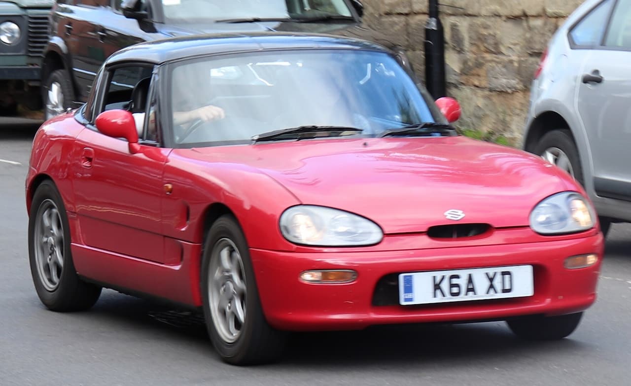 Red Suzuki Cappuccino parked on a sunny street, top down.