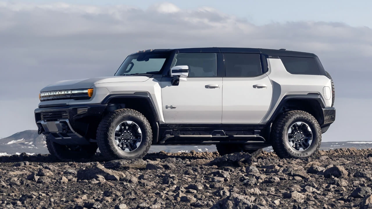 White and black 2025 GMC Hummer EV SUV with rugged design, large off-road tires, and boxy styling on rocky terrain