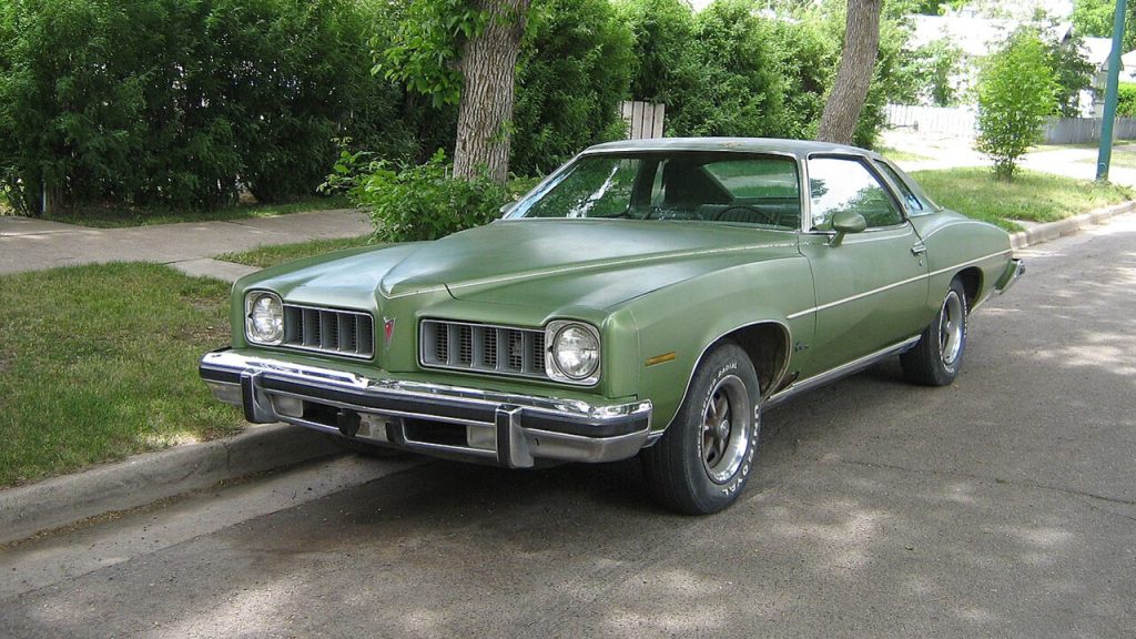 Green 1974 Pontiac LeMans classic car parked on residential street with trees and grass in background