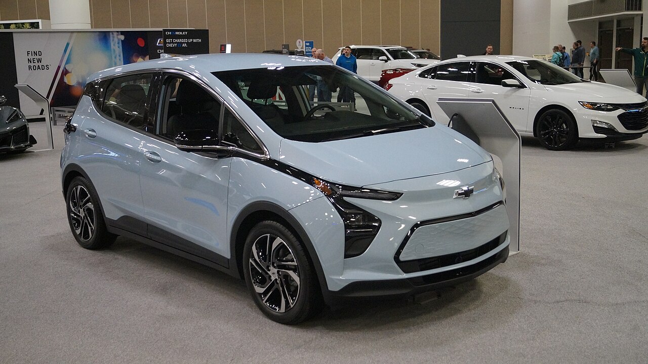 White 2023 Chevrolet Bolt EV 1LT displayed in auto show with sleek design and distinctive angular headlights