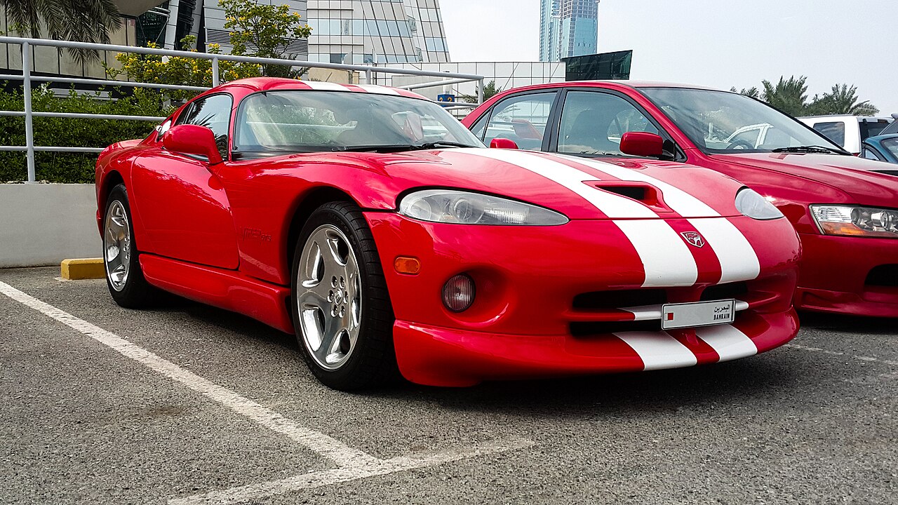 Red Dodge Viper with white racing stripes parked in urban parking lot with city buildings behind