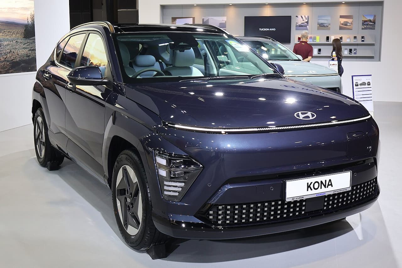 Dark blue 2025 Hyundai Kona Electric SUV with distinctive LED light bar and pixelated grille displayed in modern showroom