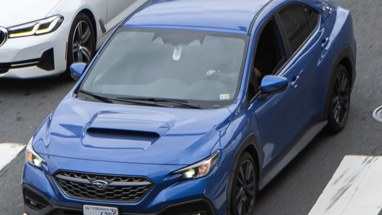 Blue 2025 Subaru WRX with hood scoop parked on road next to white BMW sedan