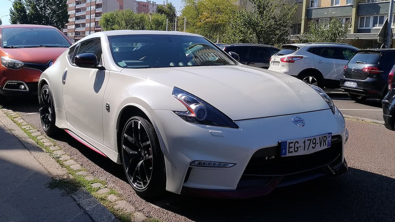White Nissan 370Z NISMO sports car parked on street with French license plate and apartment buildings behind