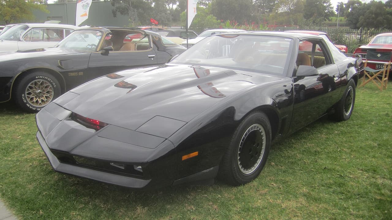 Black 1982 Pontiac Firebird Trans Am with T-top roof parked on grass at classic car show event