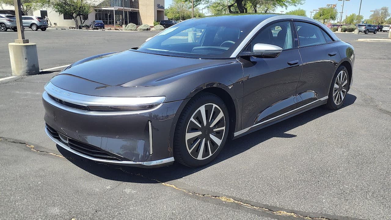 Dark gray Lucid Air Grand Touring electric vehicle parked in parking lot with distinctive front light bar and large alloy wheels