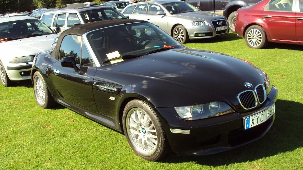 Black BMW Z3 with soft top up and European license plate parked on grass among other cars