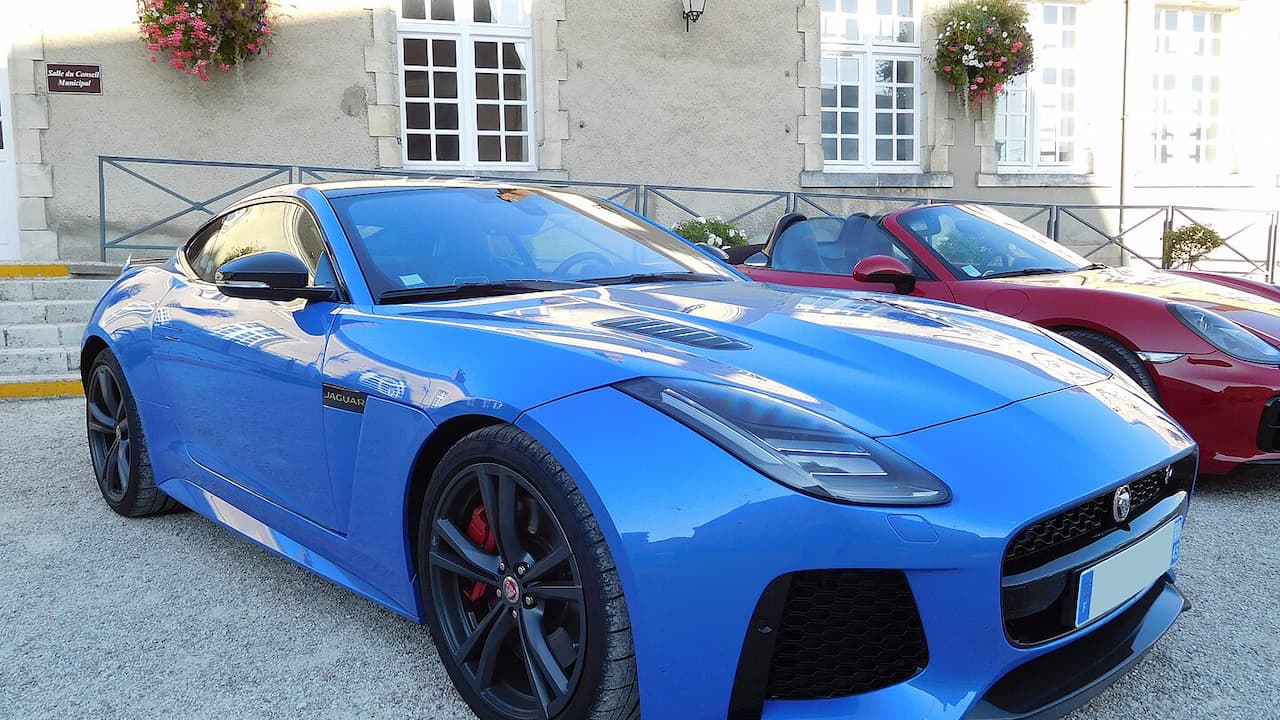 Blue Jaguar F-Type SVR coupe with black wheels, aggressive front splitter, and distinctive hood vents parked beside red car
