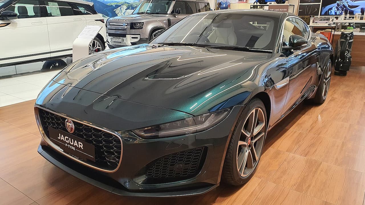 Dark green Jaguar F-Type displayed in automotive showroom with wooden floors and other vehicles visible