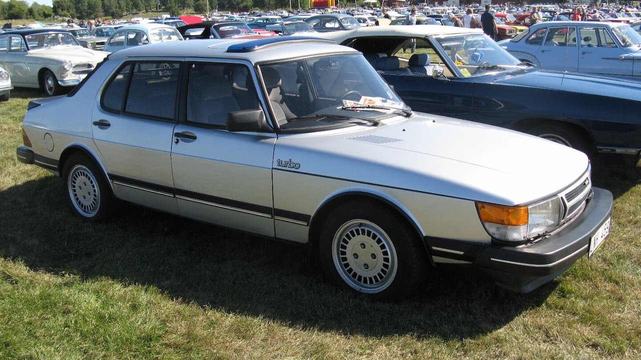 White Saab 900 Turbo with distinctive angular design parked on grass at large classic car show
