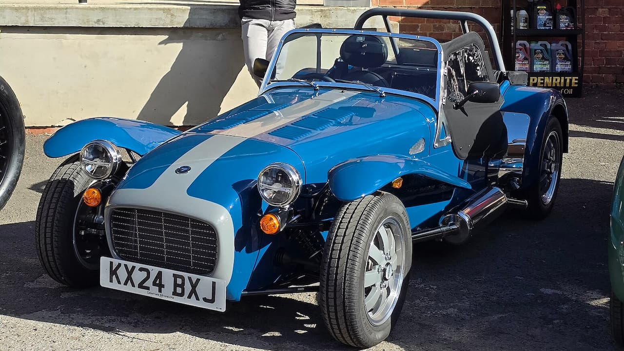Blue and white Caterham Seven lightweight sports car with exposed wheels and roll cage parked on street