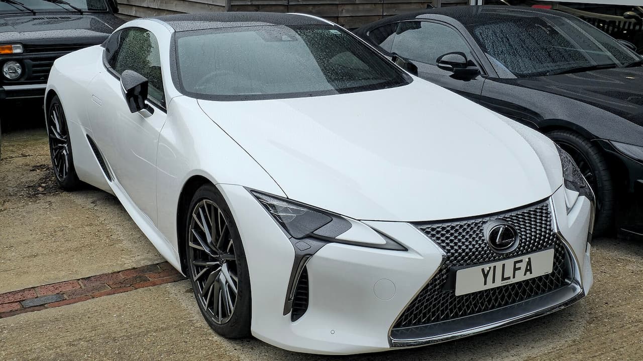 White Lexus LC with license plate "YILFA" parked among other vehicles on paved surface
