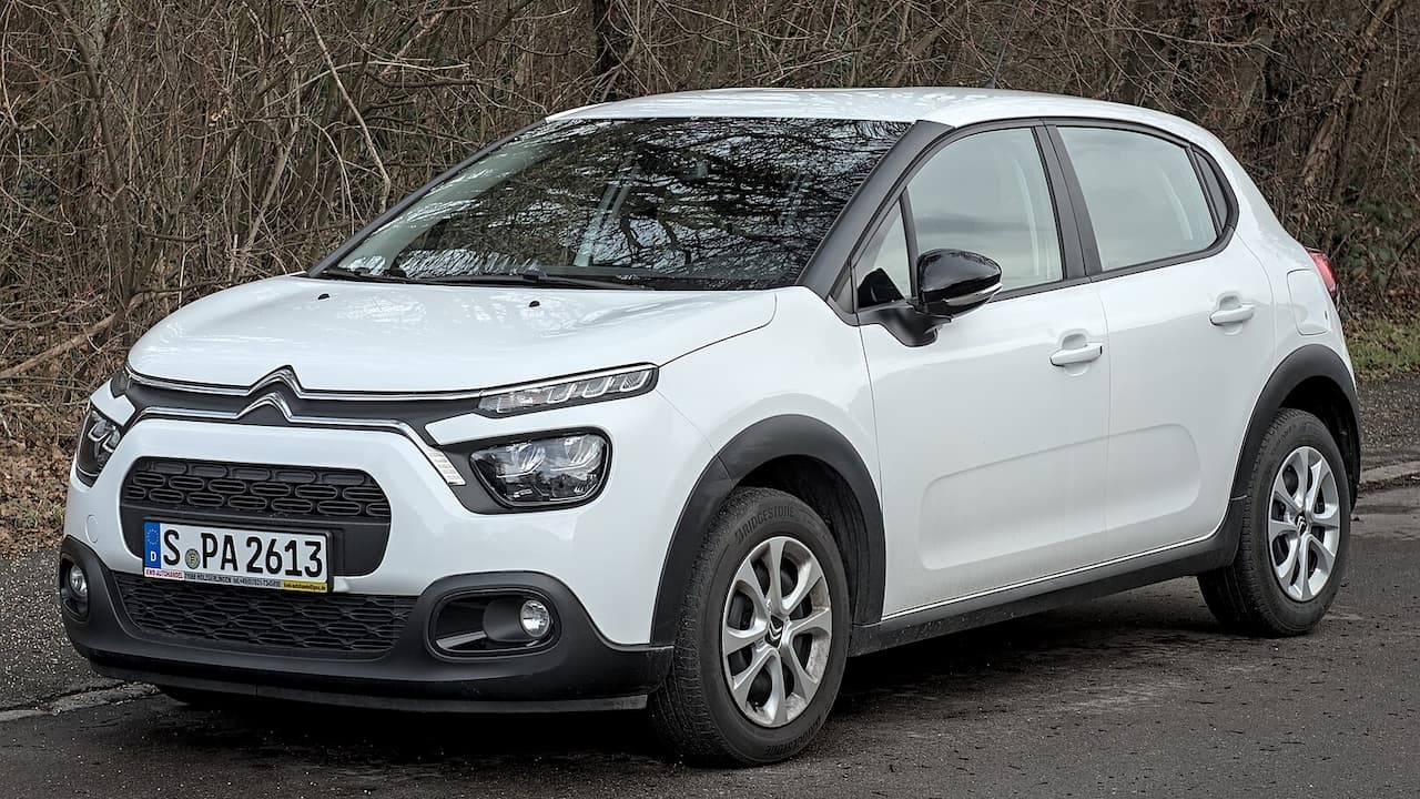 White Citroën C3 parked on asphalt road against bare winter trees, featuring distinctive front grille and black plastic cladding