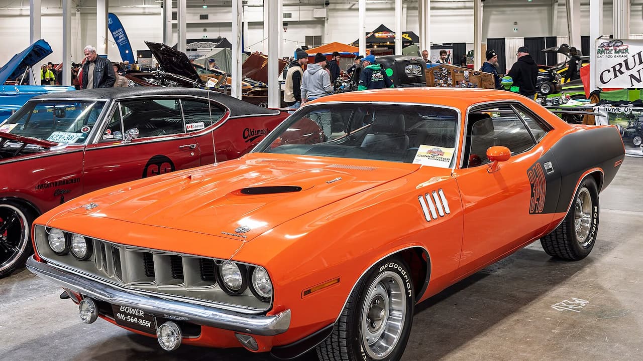 Bright orange 1971 Plymouth 'Cuda muscle car with black hood displayed at indoor classic car show