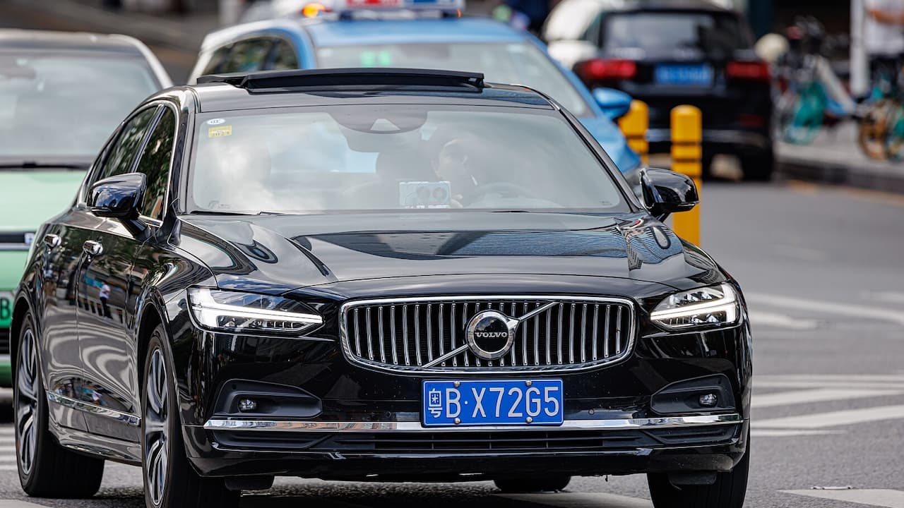 Black Volvo S90 with distinctive vertical grille and LED headlights driving on city street with blue license plate