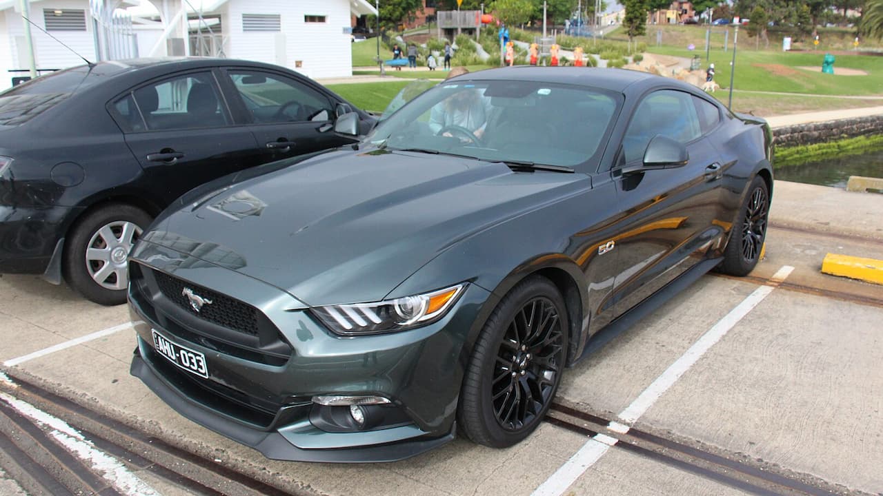 Dark gray Ford Mustang 4-cylinder with 10-speed automatic parked in lot with black wheels, orange accent stripes, and license plate