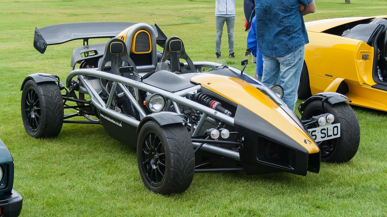 Yellow and black Ariel Atom lightweight track car with exposed tubular frame and large rear wing on grass