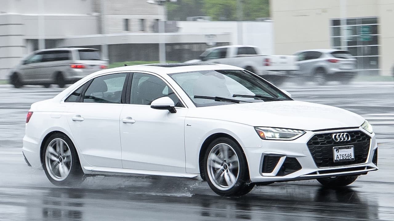 White 2025 Audi A4 driving on wet pavement with distinctive hexagonal grille and modern LED headlights