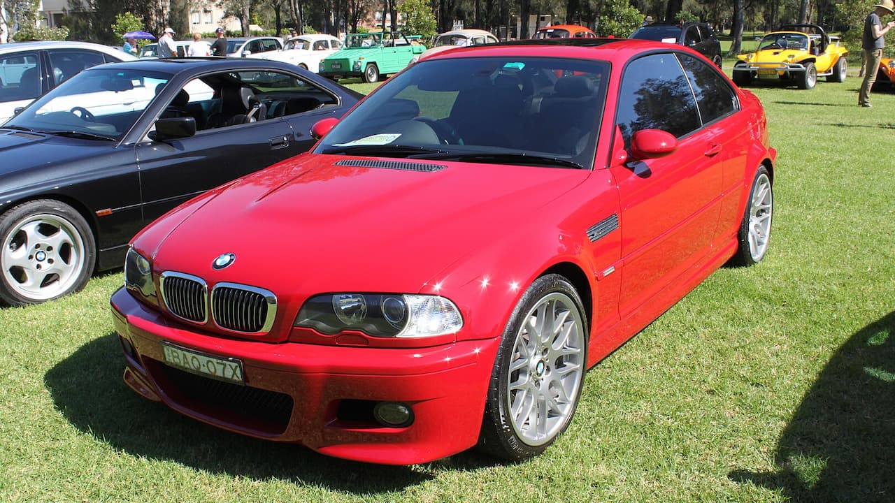 Red BMW M3 E46 at outdoor car show with classic and modern vehicles on grass field