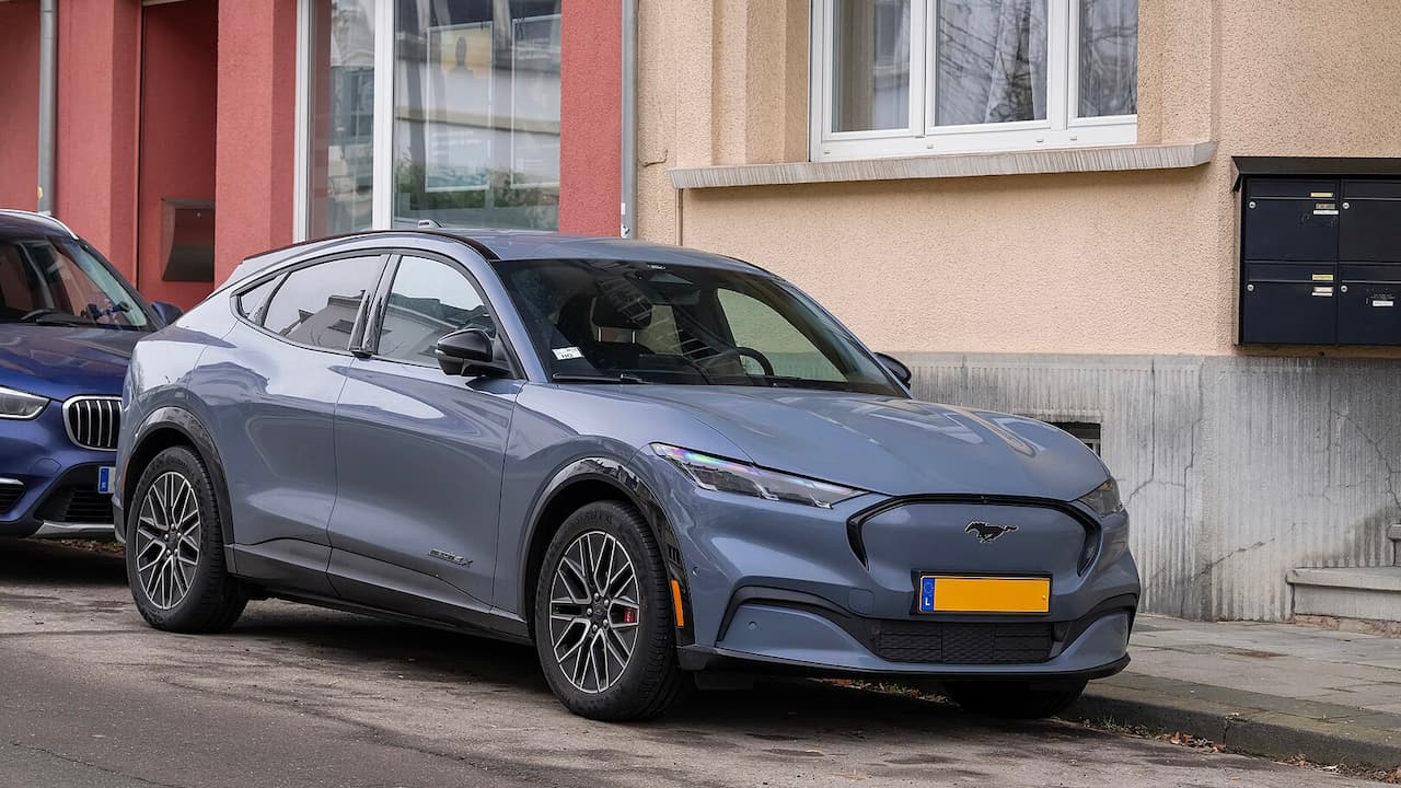 Gray 2025 Ford Mustang Mach-E electric SUV parked on street in front of colorful residential buildings