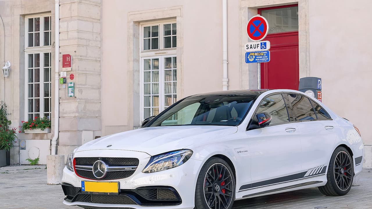 White Mercedes-AMG C63 S parked on cobblestone street in front of cream-colored European building