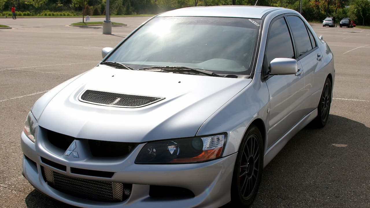 Silver Mitsubishi Lancer Evolution VIII with hood vents and dark wheels parked in empty parking lot