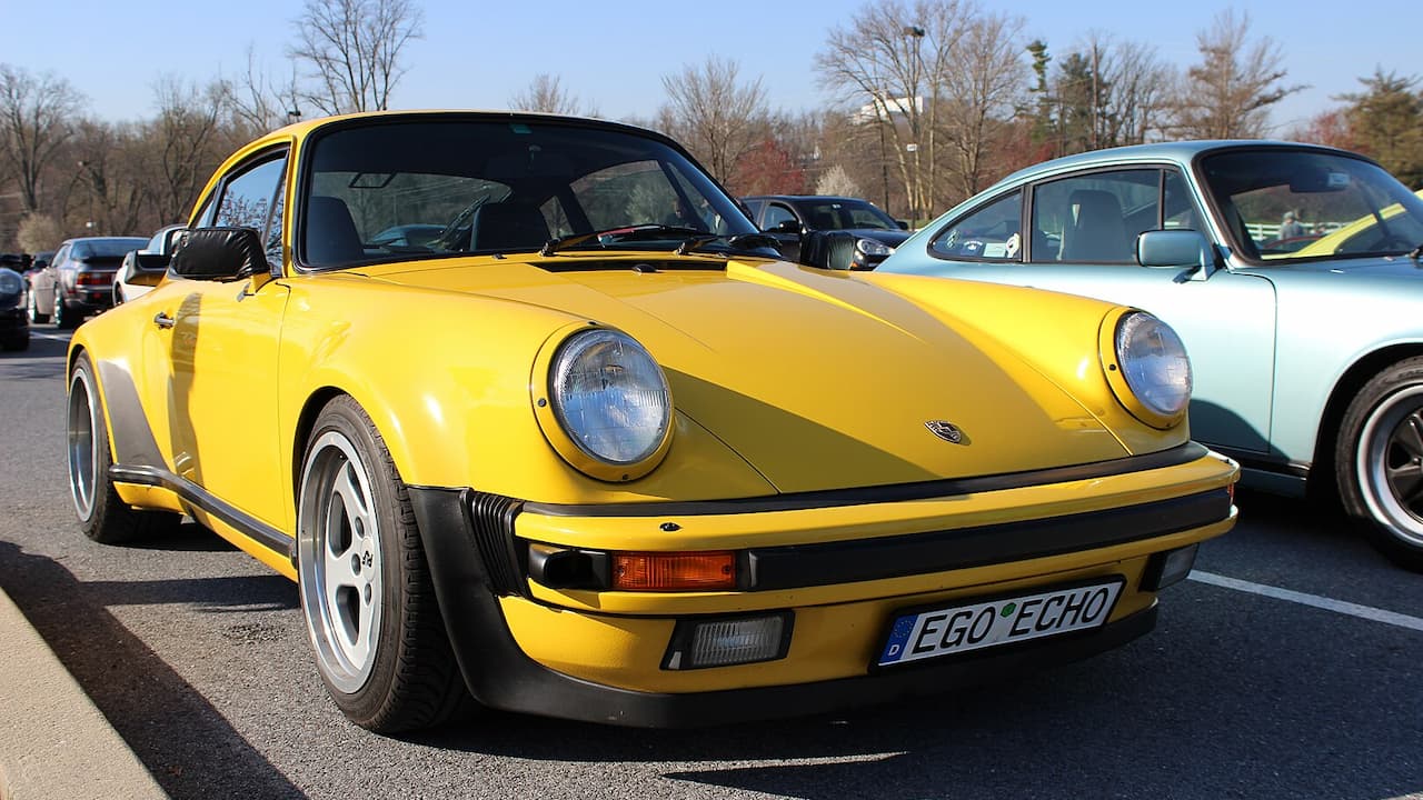 Yellow Porsche 911 (930 Turbo) with distinctive whale tail spoiler and license plate "EGO ECHO" at car meet