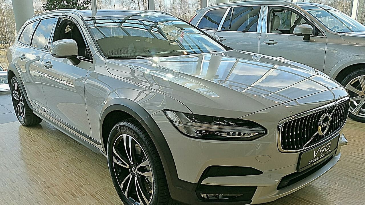 Gray Volvo V90 Cross Country parked at dealership with distinctive grille, alloy wheels, and other vehicles visible in background