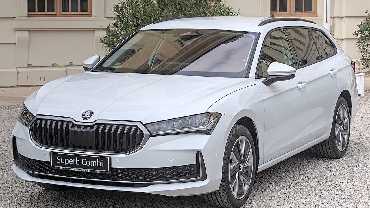 White Skoda Superb Combi parked on gravel driveway in front of modern house with large windows