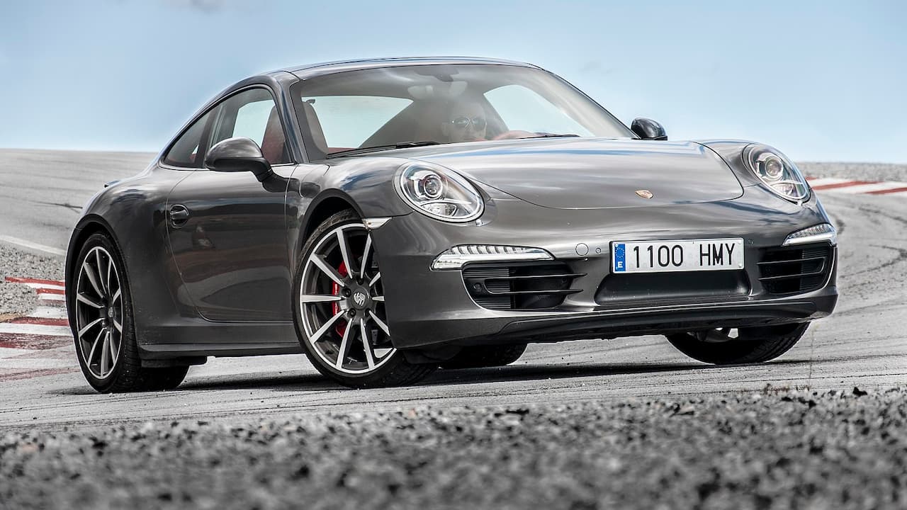 Dark gray Porsche 911 Carrera with license plate 1100 HMY parked on race track with cloudy sky background