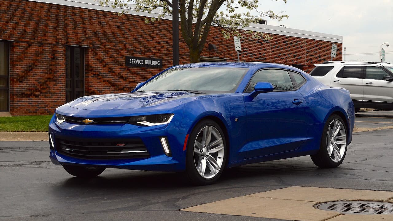 Blue Chevrolet Camaro 2.0 Turbo parked on street in front of red brick service building with tree