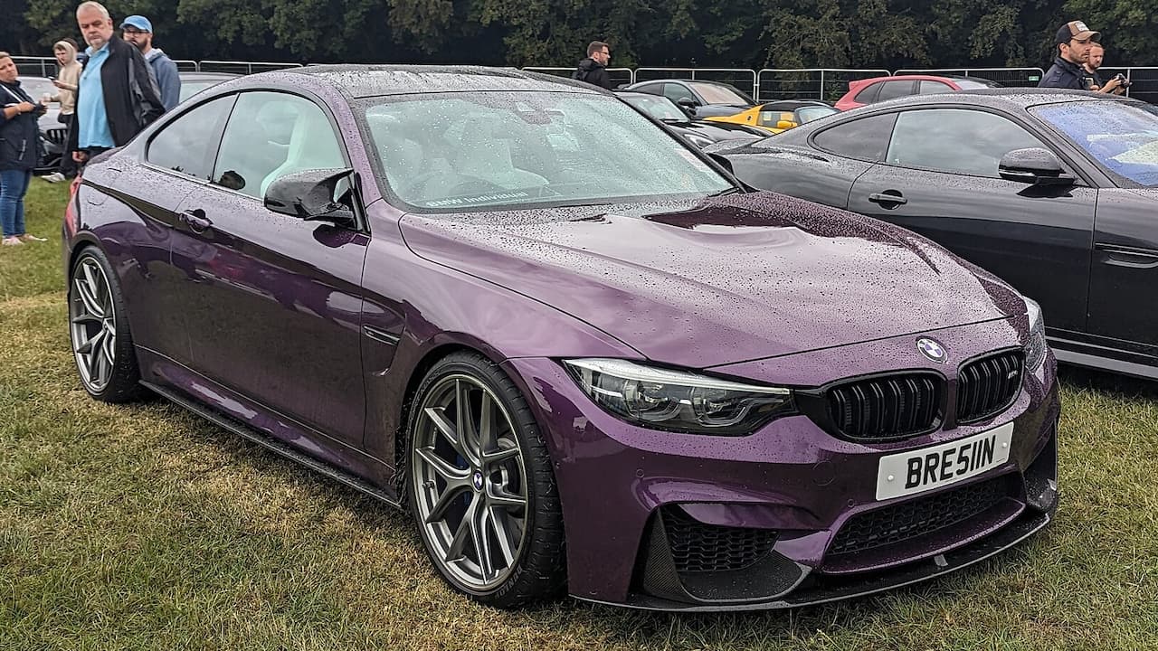 Purple BMW M4 Competition coupe with license plate "BRESLIN" parked on grass at outdoor car show event