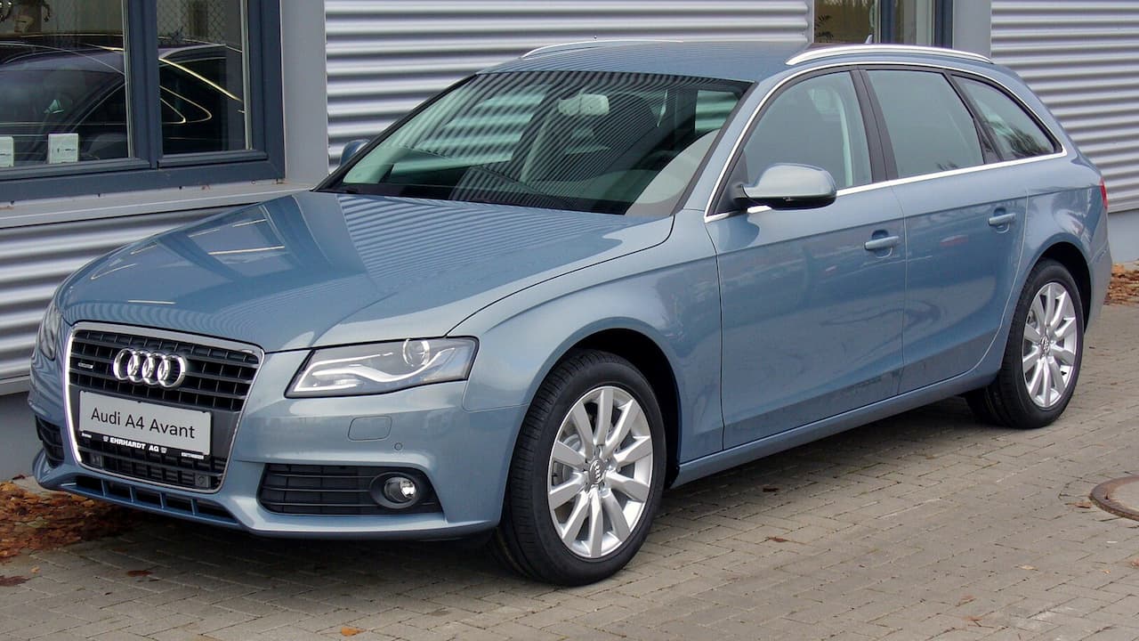 Light blue Audi A4 Avant parked at dealership with distinctive grille, alloy wheels, and corrugated metal building behind