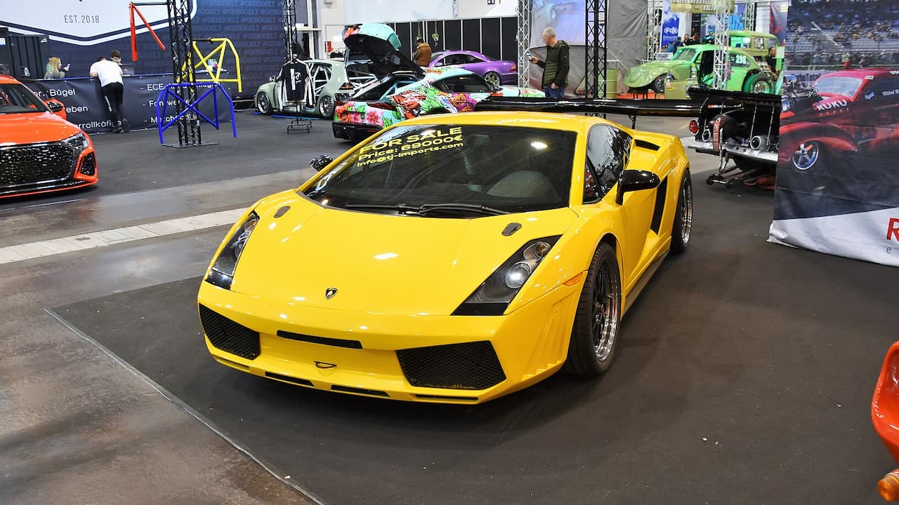 Yellow Lamborghini Gallardo 6-Speed displayed at indoor car show with other exotic vehicles and exhibition stands around