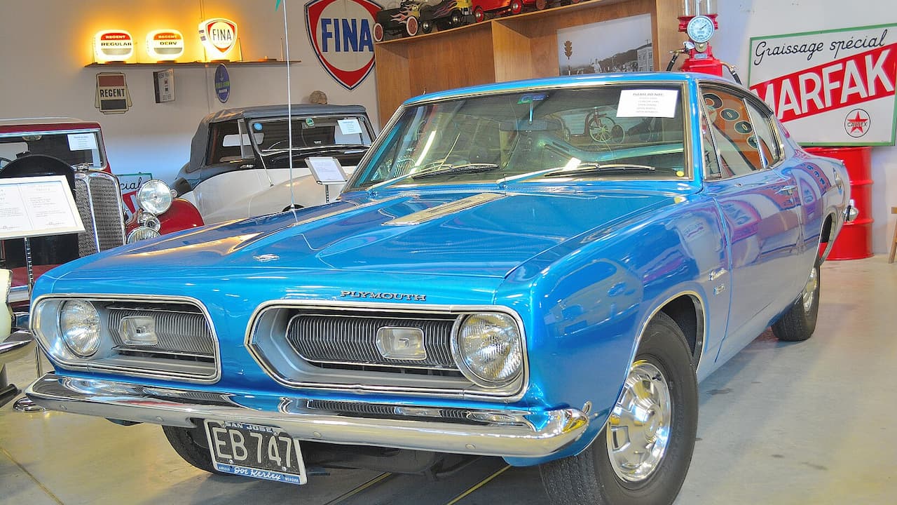 Bright blue 1968 Plymouth Barracuda displayed in indoor automotive museum with vintage gas station signs and memorabilia