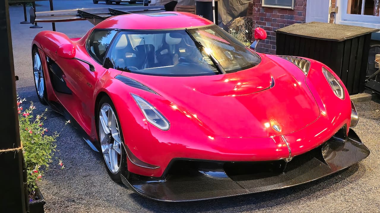 Bright red Koenigsegg Jesko with large rear wing and carbon fiber aerodynamic elements parked outdoors