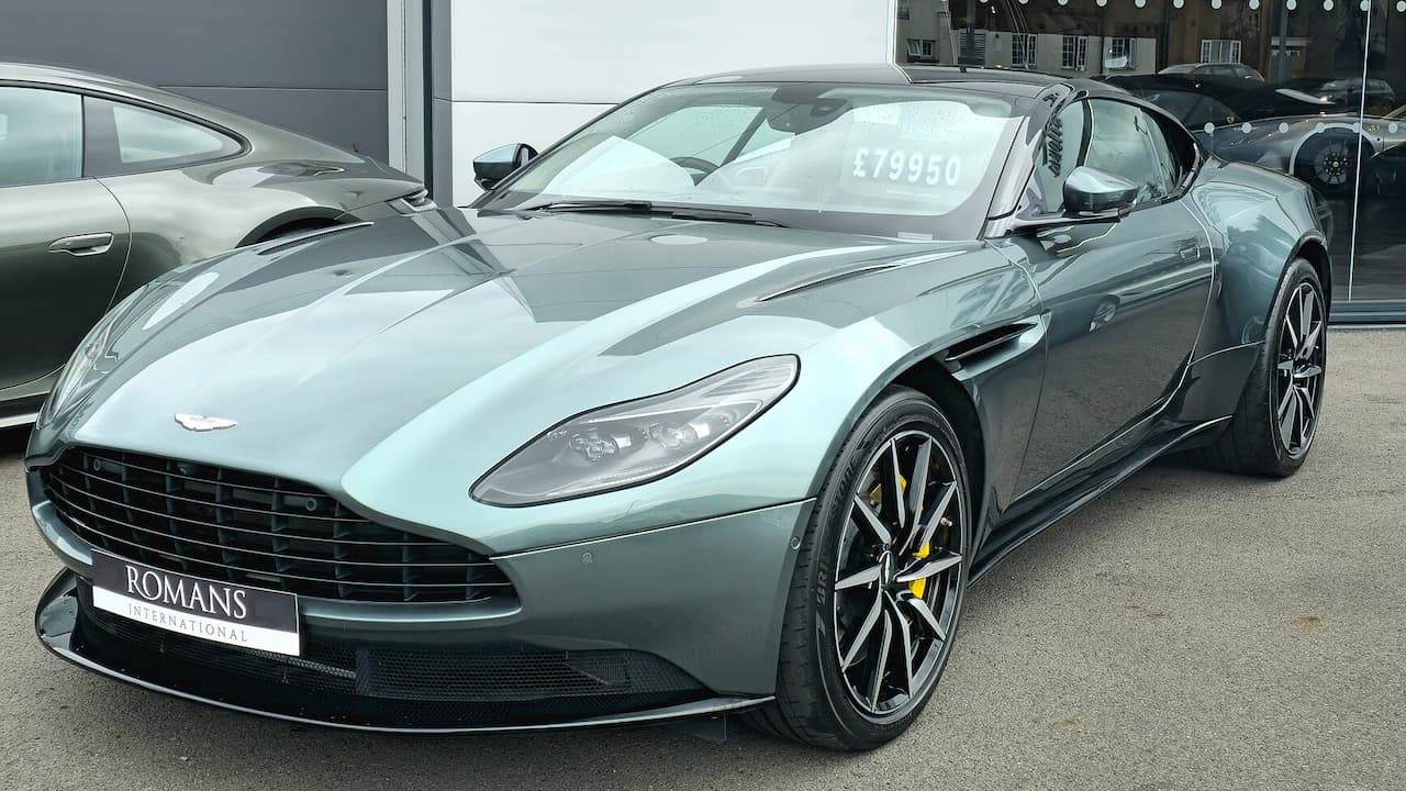 Aston Martin DB11 with distinctive grille, sporty alloy wheels, and yellow brake calipers at dealership