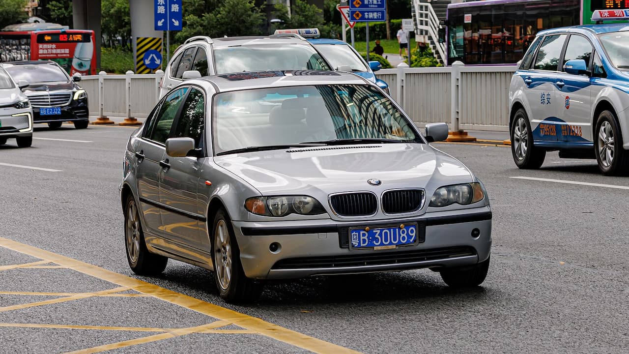 Silver BMW 3 Series E46 driving on Chinese city street with blue license plate and distinctive kidney grille