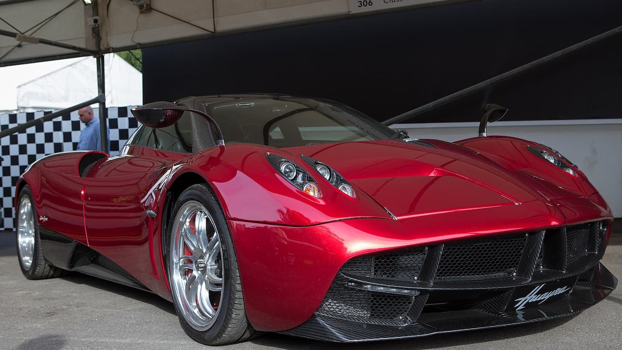 Red Pagani Huayra with distinctive gull-wing doors and chrome wheels displayed under white tent at car show