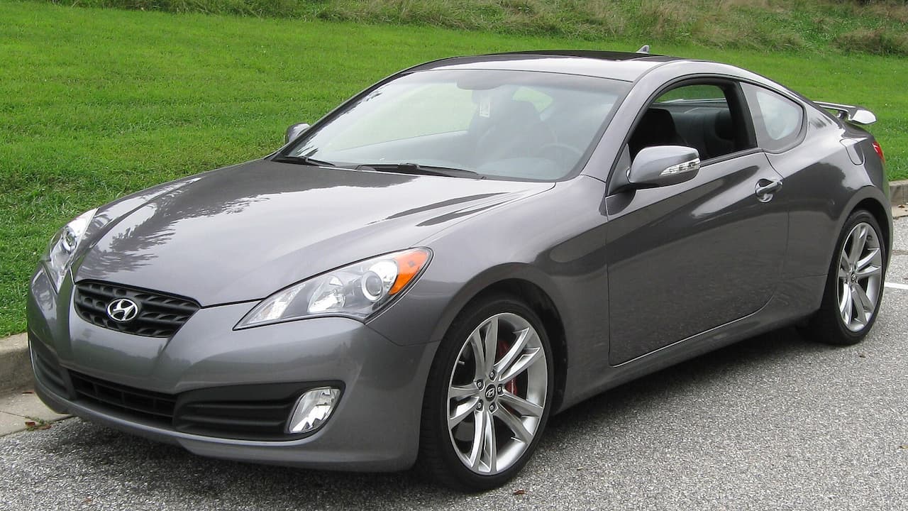 Gray Hyundai Genesis Coupe parked on asphalt road with green grass field in the background